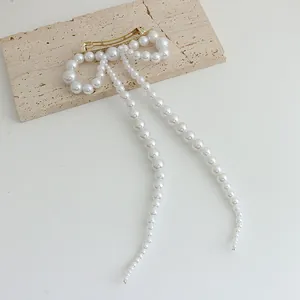 Détail d'une pince à cheveux avec nœud en perles et élégants pompons sur base dorée