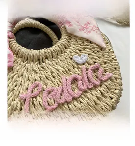 Detail of round straw bag with pink rope embroidery and floral scarf on handle