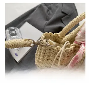 Close-up of woven straw tote bag featuring silver hardware and a decorative silk scarf