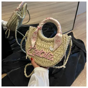 Close-up of woven straw handbag with pink Lalala embroidery and silk scarf handle