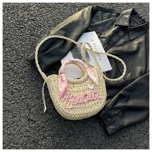 Straw tote bag detail with pink knit letters, floral silk scarf, and long shoulder strap