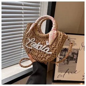 Detailed macro view of woven straw bag with white Lala embroidery and floral silk scarf