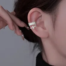 Close-up of silver ear cuff with square zircons and dangling cross pendant detail