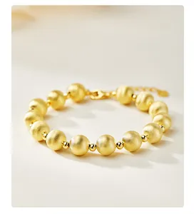 Détail d'un bracelet en perles dorées avec perles œil de chat mates et fermoir homard