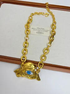 Detail of vintage gold evil eye pendant with surrealist face and blue eye on a thick chain