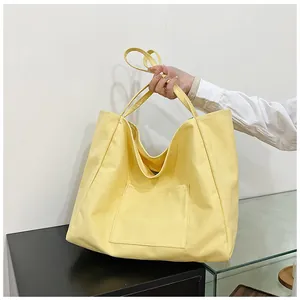 Detail of a bright yellow canvas tote bag featuring an external front pocket and long straps