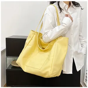 Side view of a bright yellow canvas tote bag with a large front pocket worn by a model