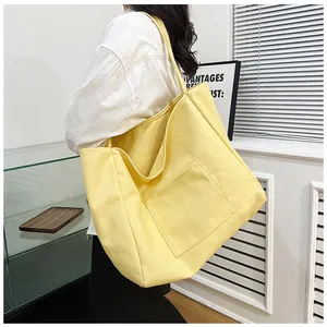 Detail of a large yellow canvas tote bag with front pocket shown in a shoulder carry style