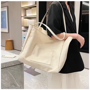 Detail of off-white canvas tote bag featuring a square front pocket and wide strap