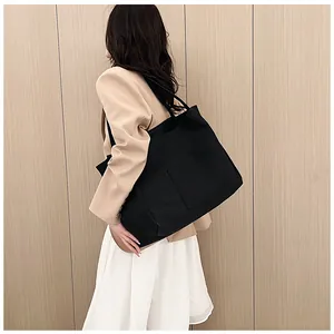 Close-up of a large black canvas tote bag with front pocket shown on a female model