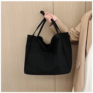 Detailed view of black canvas tote bag with front pocket held by model in beige suit
