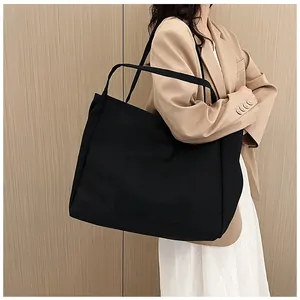 Detail shot of a black large canvas tote bag with functional front pocket on a model