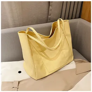Detail of a beige canvas tote bag with large front pocket on a grey fabric sofa