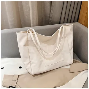 Detail of off-white canvas tote bag with front pocket on gray sofa for daily use