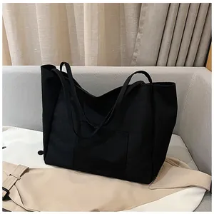 Detail of a large black canvas tote bag with front pocket on a neutral sofa background