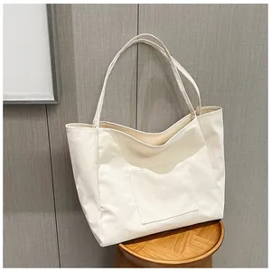 Detail of a large off-white canvas tote bag with front pocket on a wooden stool