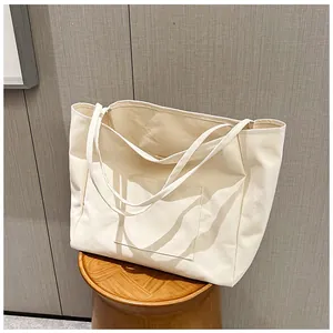 Detail of minimalist cream canvas tote bag with functional front pocket on a wooden stool