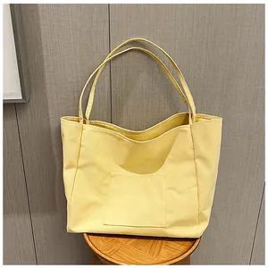 Detail of a bright yellow canvas tote bag with a front pocket on a wooden stool