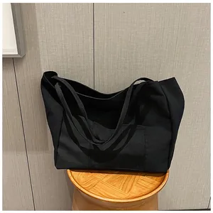 Close-up of black canvas tote bag with outer pocket on a wooden stool detail