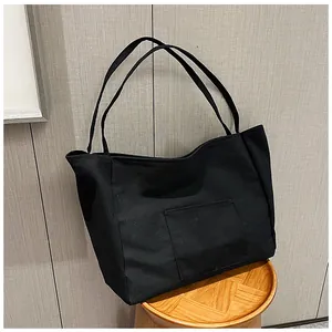 Detail shot of a black canvas tote bag with front pocket and slim shoulder straps