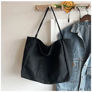 Detail of minimalist black canvas tote bag showing front pocket hanging on wooden hook