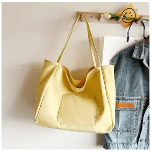 Detail of light yellow canvas tote bag with outer pocket hanging on a wooden hook
