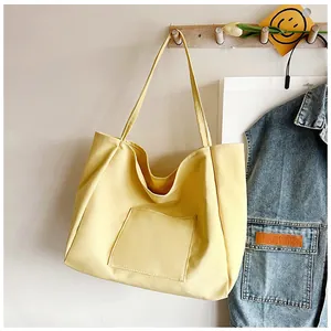 Detailed view of yellow canvas tote bag with front pocket hanging on a wooden hanger