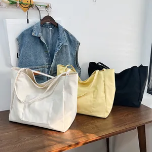Three canvas tote bags in cream, yellow, and black with large front pockets and long handles