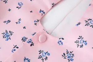 Makroaufnahme eines rosa floralen Chiffon-Oberteils mit stoffbezogenem Knopfdetail