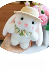 Close-up of cute white plush bunny with yellow hat and floral bow tie held in hand