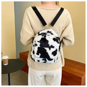 Close-up of small plush backpack with cow print pattern and metal hooks on back