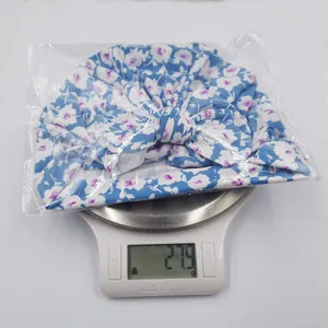 Digital scale showing newborn floral bow hat weight approximately 27.9 grams