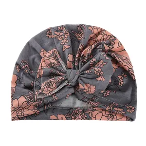 Close-up of baby turban hat with pink floral print and a large grey bow on white background
