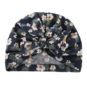 Detail of floral printed baby turban hat with a large navy blue bow in soft cotton