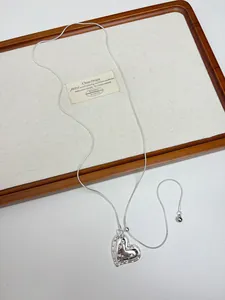 Close-up detail of a minimalist silver metallic heart pendant necklace on a wooden tray