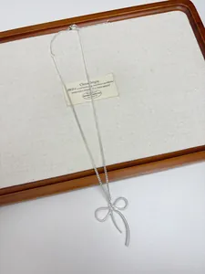 Close-up of a minimalist silver bow pendant necklace on a wooden display tray.