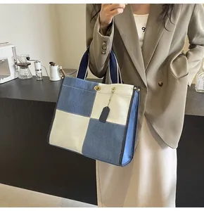 Detail of blue denim patchwork tote bag with brass twist lock held by a model
