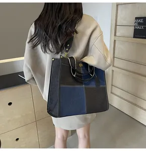 Detail of blue denim tote bag with rivets and wide strap shown on a beige hoodie