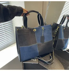 Detail of blue and black patchwork denim tote bag with leather handles and gold clasp