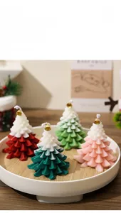Detail of four colorful gradient Christmas tree candles with golden bells in a white tray