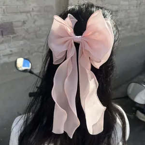 Pink oversized organza bow hair clip with elegant long ribbons on dark hair