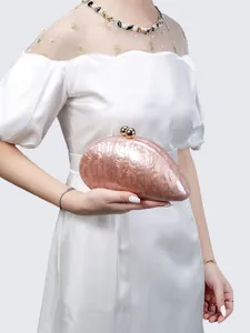 Detail view of a shell-shaped acrylic evening clutch with pink pearlescent marble finish