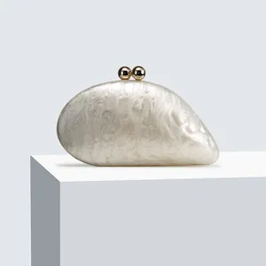 Macro view of pearl white acrylic evening clutch with gold spherical clasp and marble texture