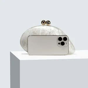 Detailed view of pearlescent white acrylic evening clutch next to a phone for size