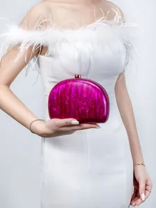 Detail of fuchsia marble acrylic evening clutch bag with gold clasp held by a model