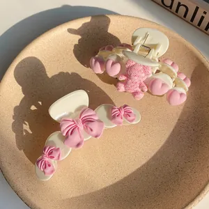 Close-up of cream hair claws with pink bear and bow details in a matte ceramic tray