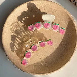 Detail of peach hair claws with pink 3D fruit designs on white and clear bases