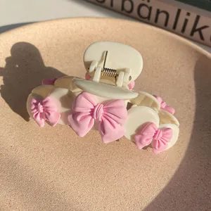 Close-up of cream white hair claw clip featuring pink bows and gold metal spring detail