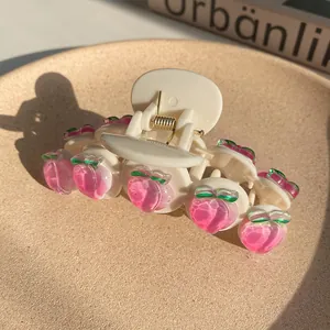 Detail of cream hair claw clip featuring pink peach charms and gold metal spring