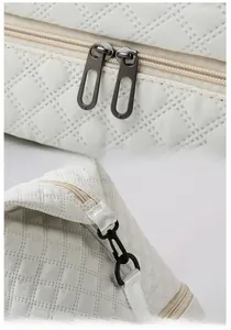 Detail view of gunmetal hardware, dual zippers, and quilted nylon on the white travel bag